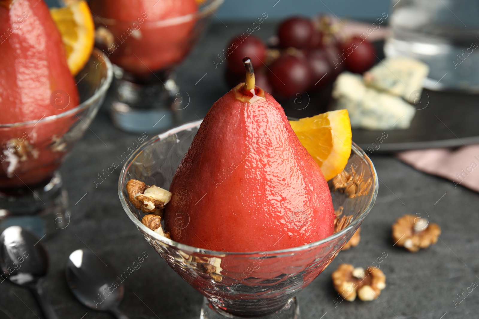 Photo of Glass bowl with red wine poached pear on grey table, closeup