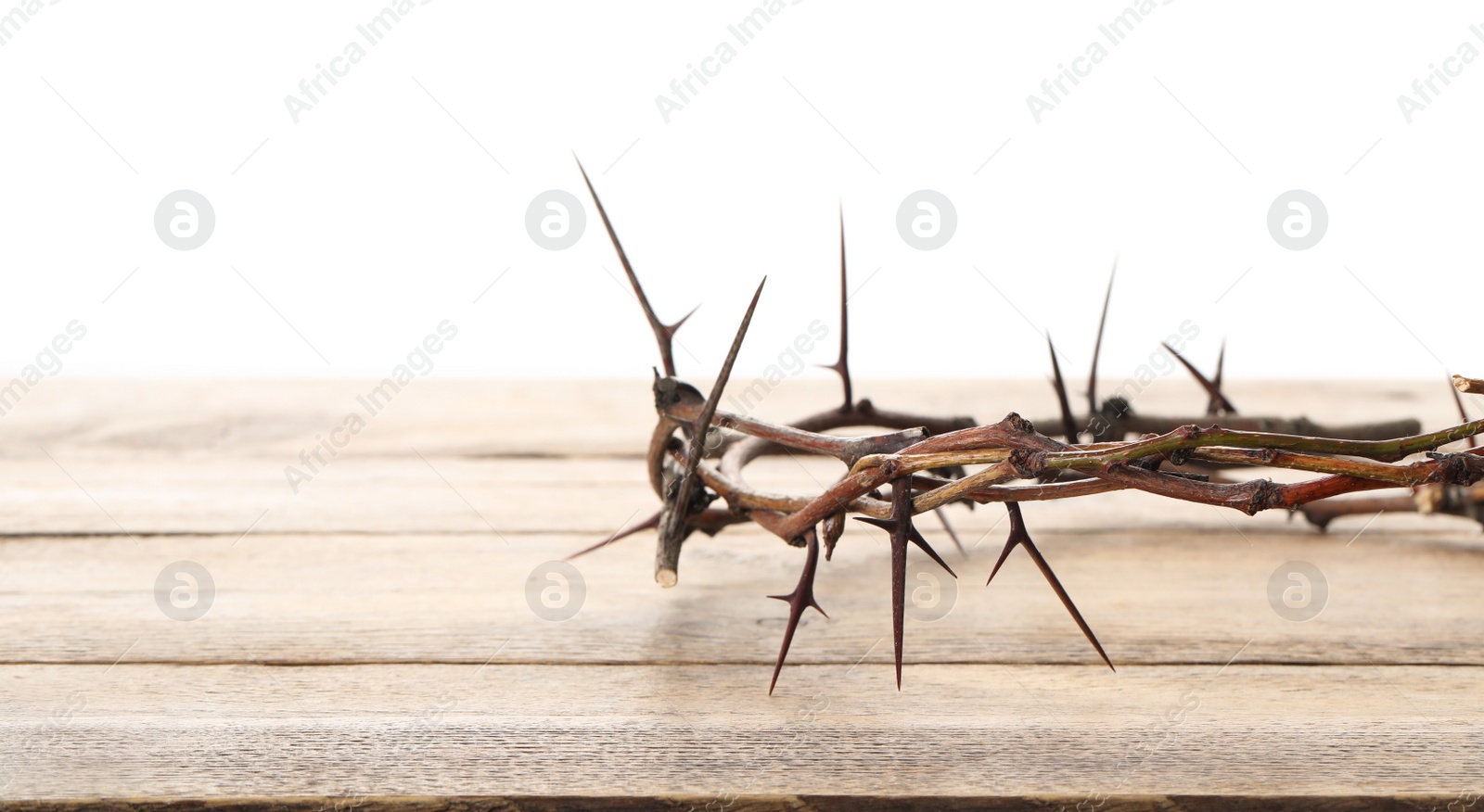 Photo of Crown of thorns on wooden table against white background, closeup with space for text. Easter attribute