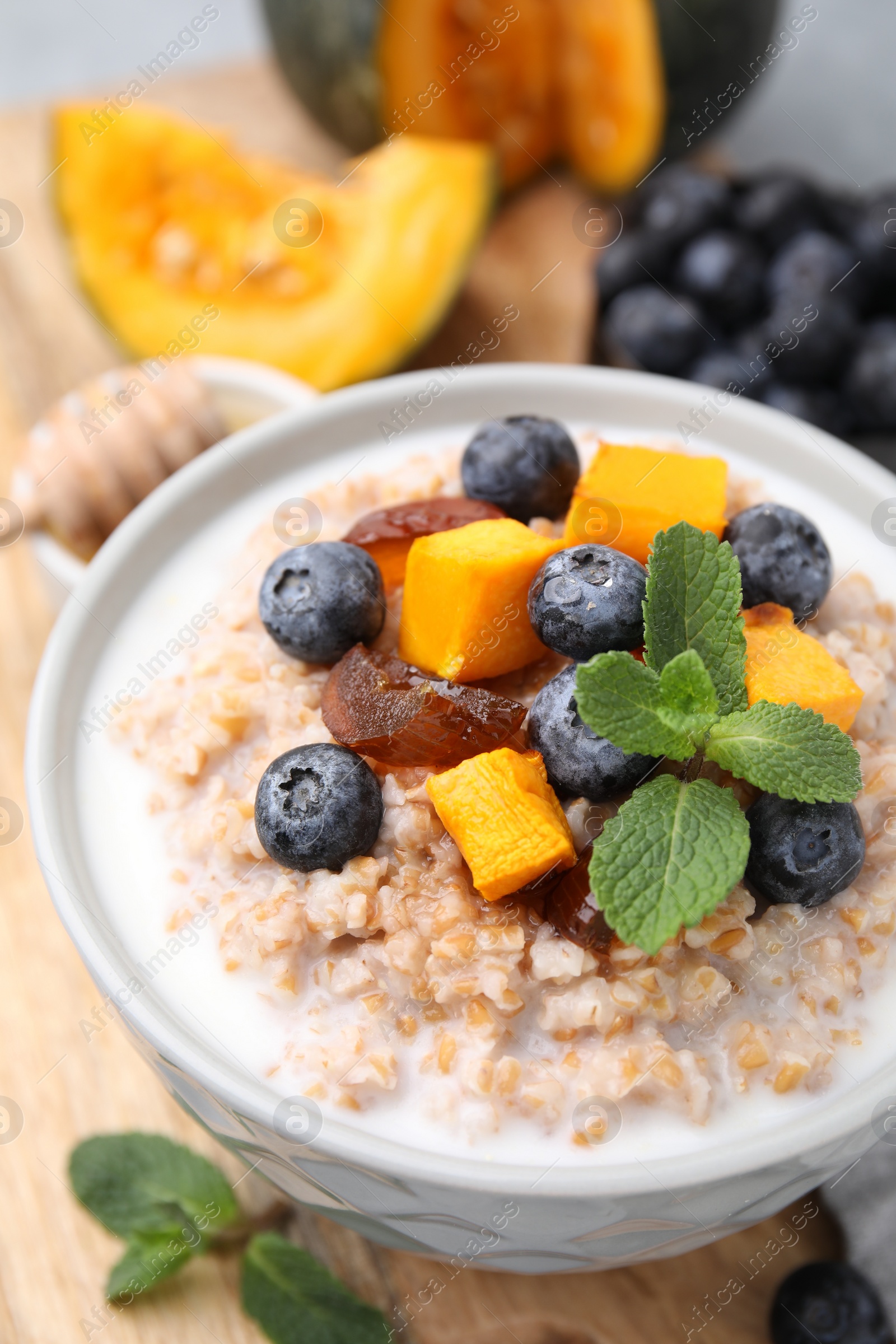 Photo of Tasty wheat porridge with pumpkin, dates and blueberries in bowl on table, closeup