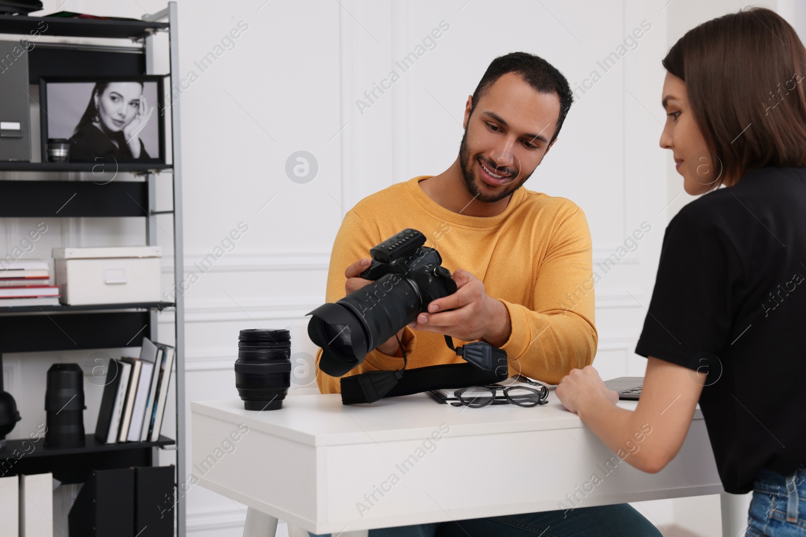 Photo of Young professional photographer showing camera to woman in modern photo studio