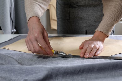 Photo of Tailor transferring sewing pattern onto fabric with tracing wheel in atelier, closeup