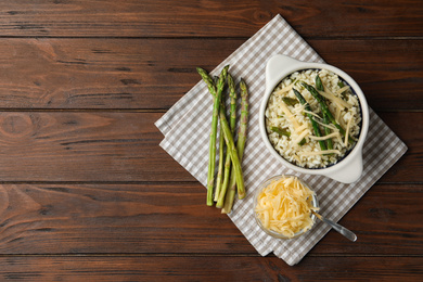 Photo of Delicious risotto with asparagus served on wooden table, flat lay. Space for text