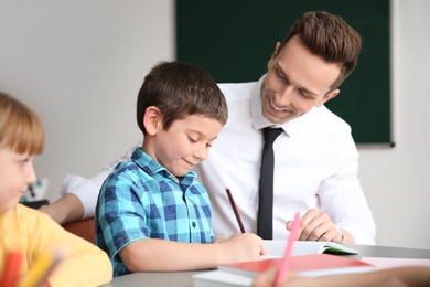 Photo of Male teacher helping boy with his task in classroom at school