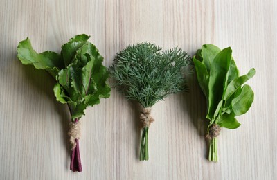 Photo of Bunches of beet leaves, dill and sorrel on white wooden table, flat lay