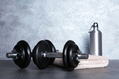 Photo of Pair of adjustable dumbbells with towel and bottle on floor indoors