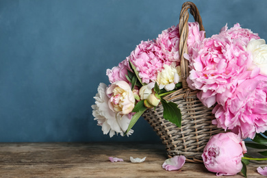 Beautiful peonies in wicker basket on wooden table. Space for text