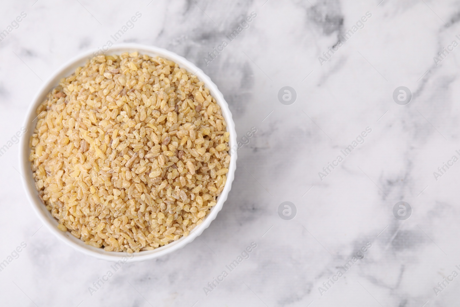 Photo of Raw bulgur in bowl on marble table, top view. Space for text