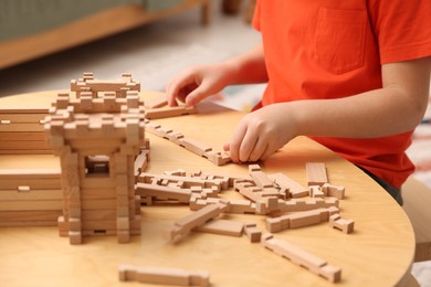 Little boy playing with wooden construction set at table in room, closeup. Child's toy