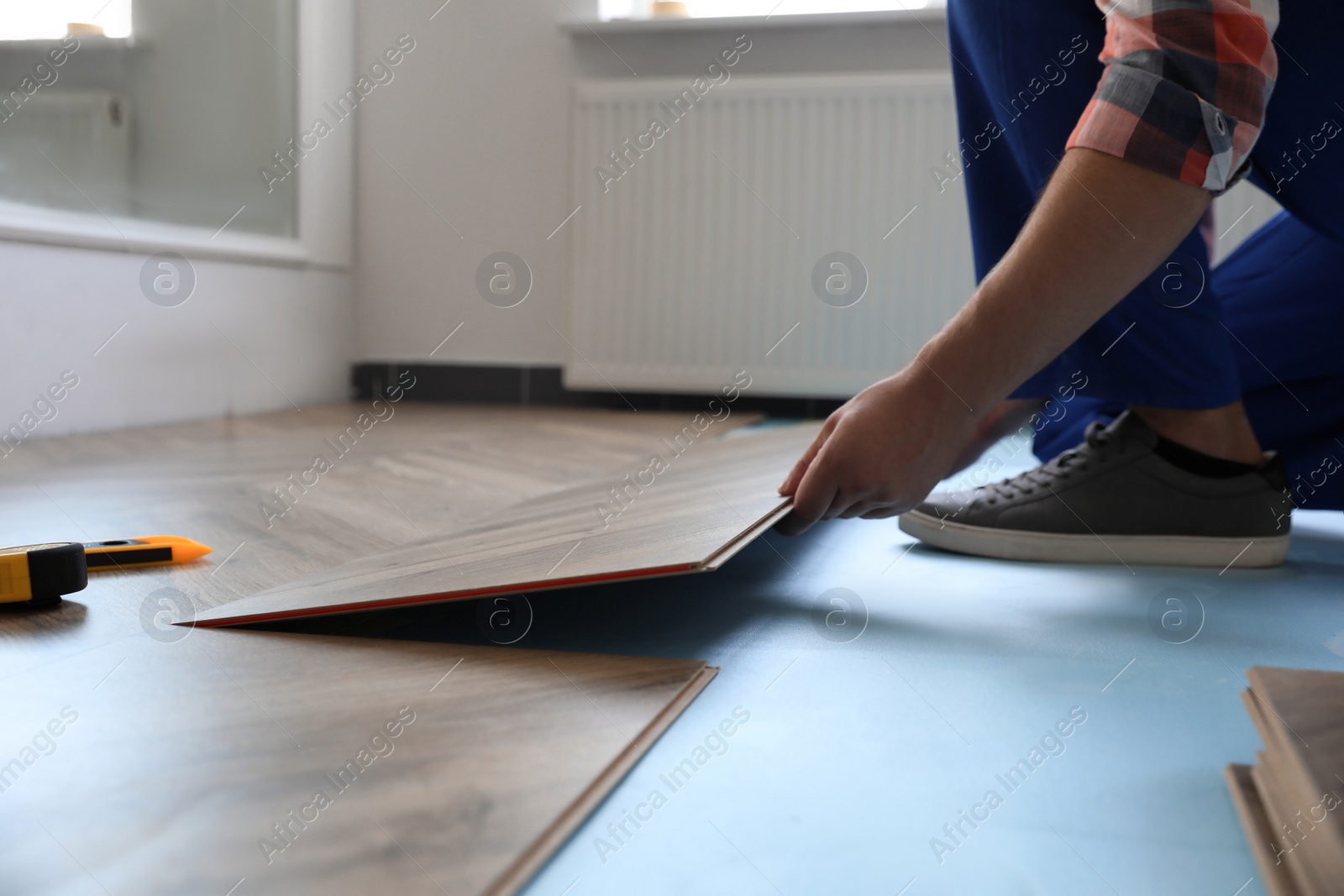 Photo of Worker installing laminated wooden floor indoors, closeup