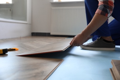 Worker installing laminated wooden floor indoors, closeup