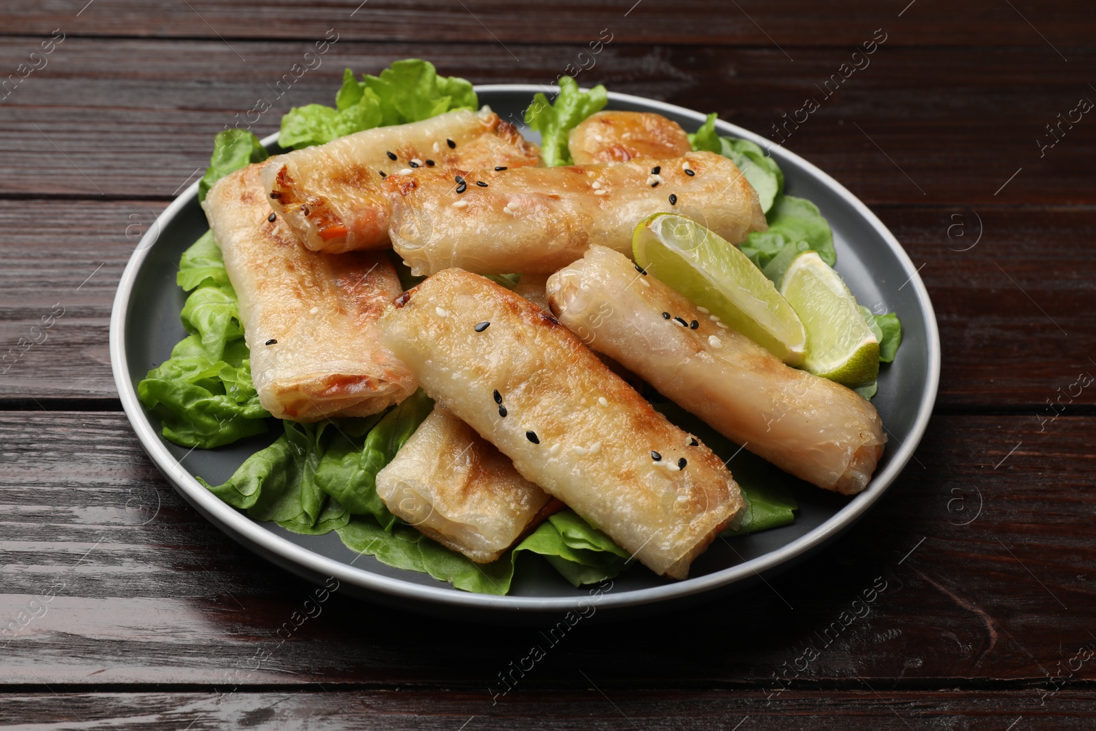 Photo of Tasty fried spring rolls, lettuce and lime on wooden table