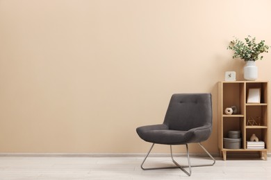 Photo of Living room interior with comfortable armchair and shelving unit near beige wall indoors. Space for text