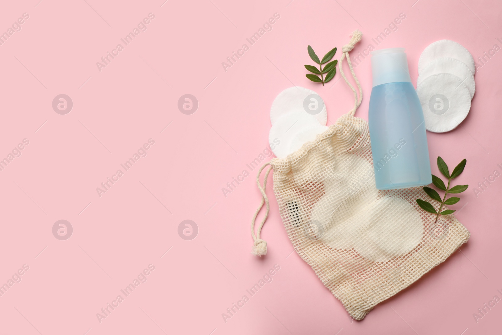 Photo of Cotton pads, leaves and makeup removal product on pink background, flat lay. Space for text