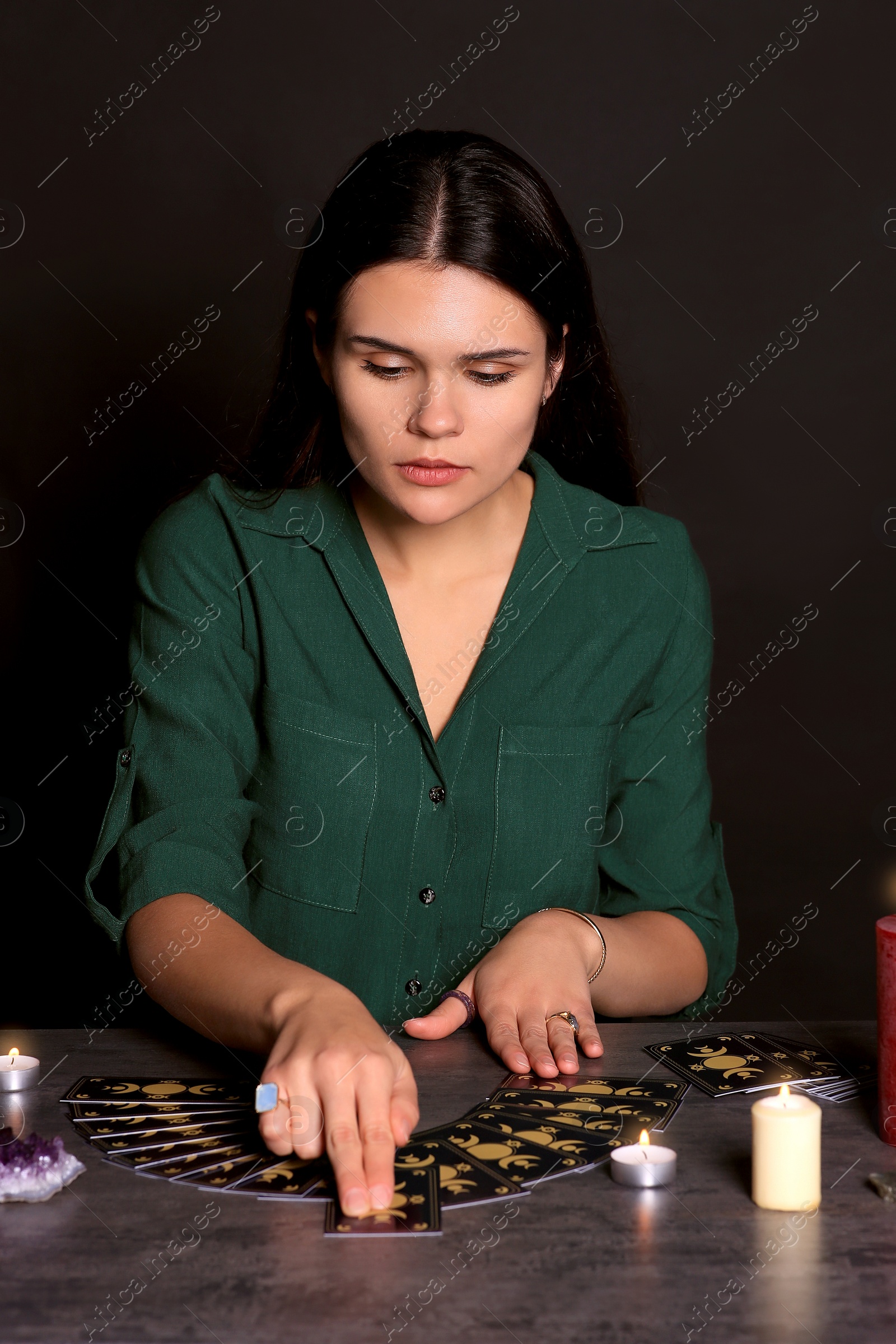 Photo of Soothsayer predicting future with tarot cards at table on black background