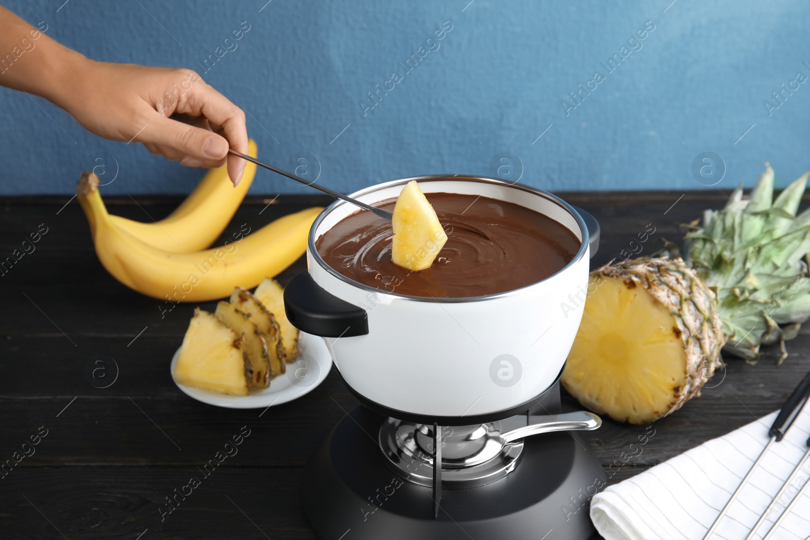 Photo of Woman dipping pineapple into pot with chocolate fondue on table, closeup