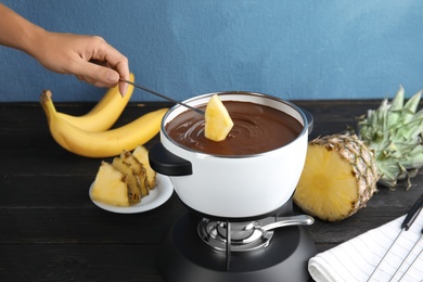 Photo of Woman dipping pineapple into pot with chocolate fondue on table, closeup