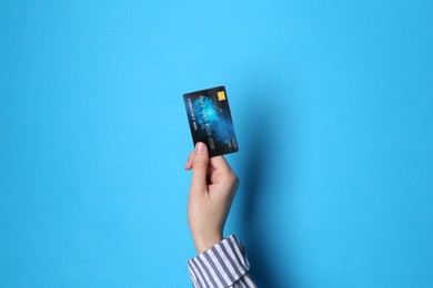 Photo of Woman holding credit card on light blue background, closeup