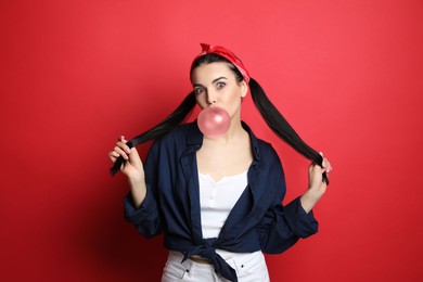 Fashionable young woman in pin up outfit blowing bubblegum on red background