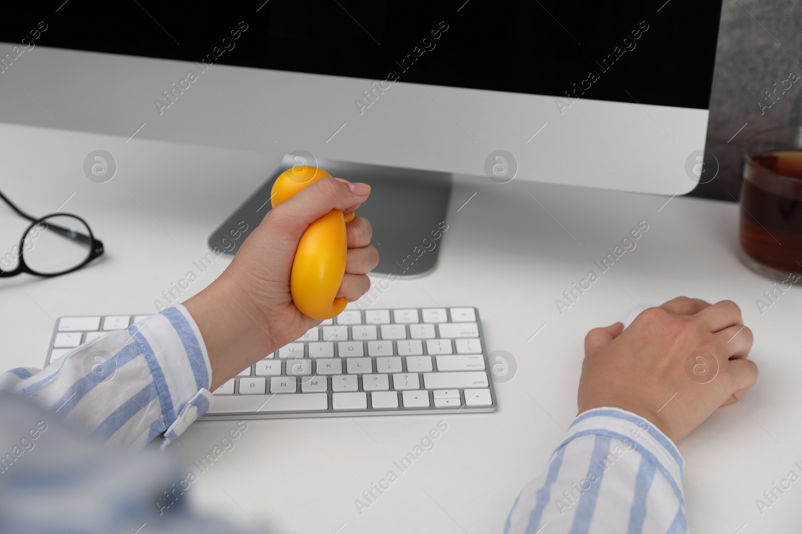 Photo of Woman squeezing antistress ball while working on computer in office, closeup