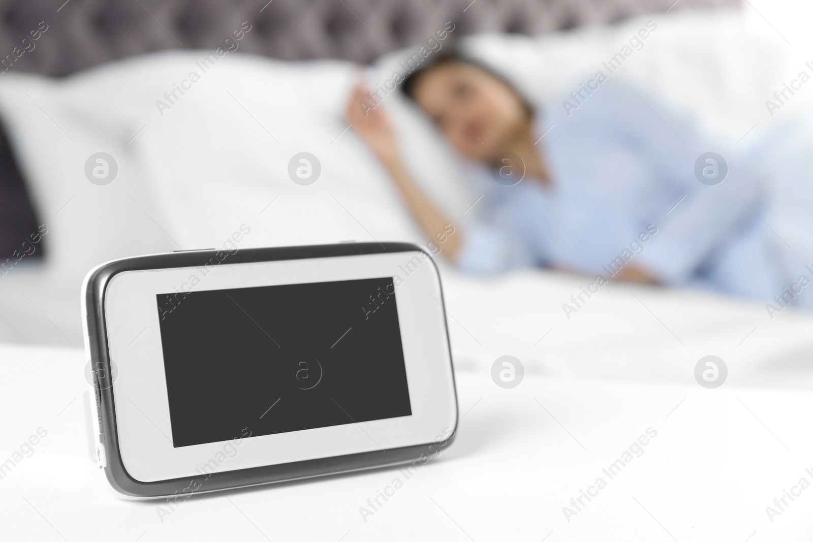 Photo of Baby monitor on table near bed with woman in room. Video nanny