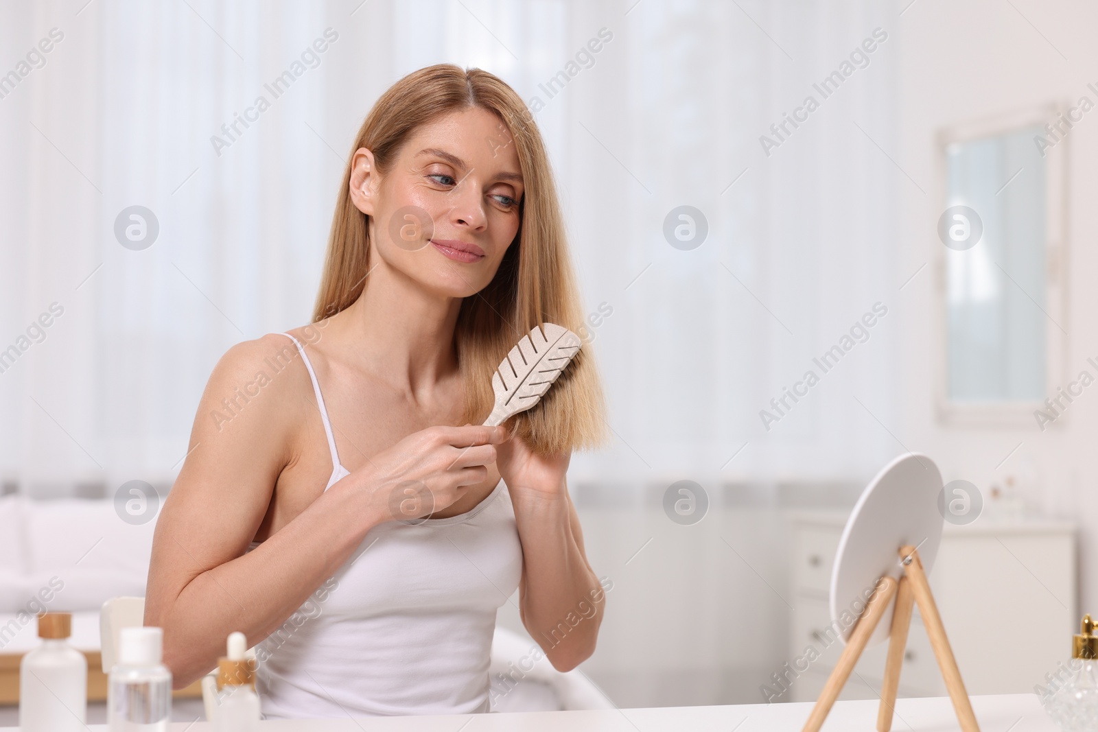 Photo of Beautiful woman brushing her hair at vanity in bedroom. Space for text