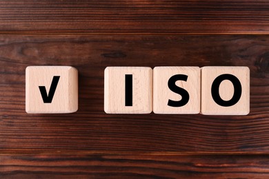 Photo of Cubes with check mark and abbreviation ISO on wooden table, flat lay