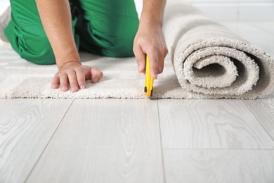 Photo of Man cutting new carpet flooring indoors, closeup. Space for text