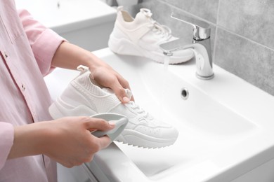 Woman washing stylish sneakers with brush in sink, closeup