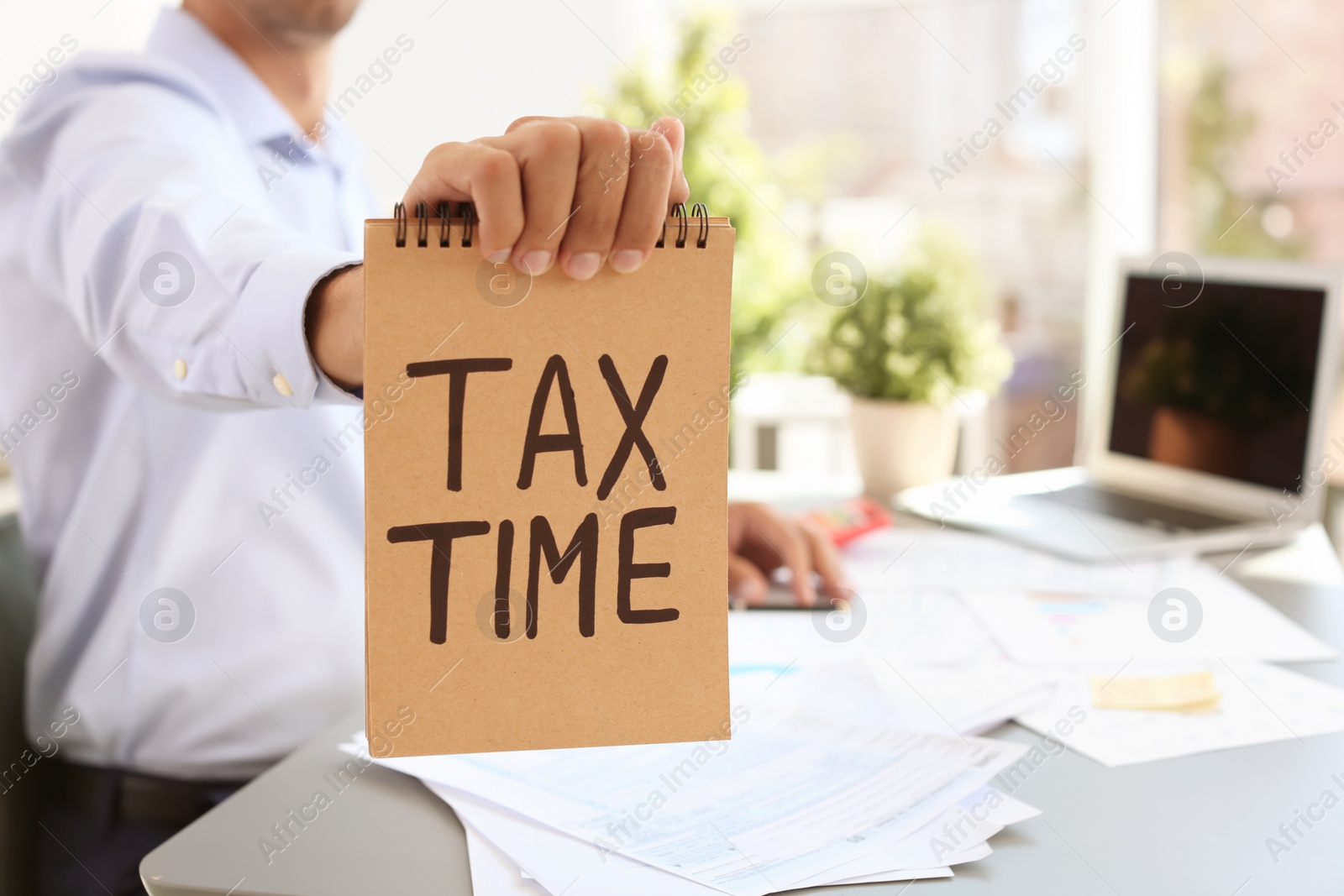 Photo of Man holding notebook with words TAX TIME indoors