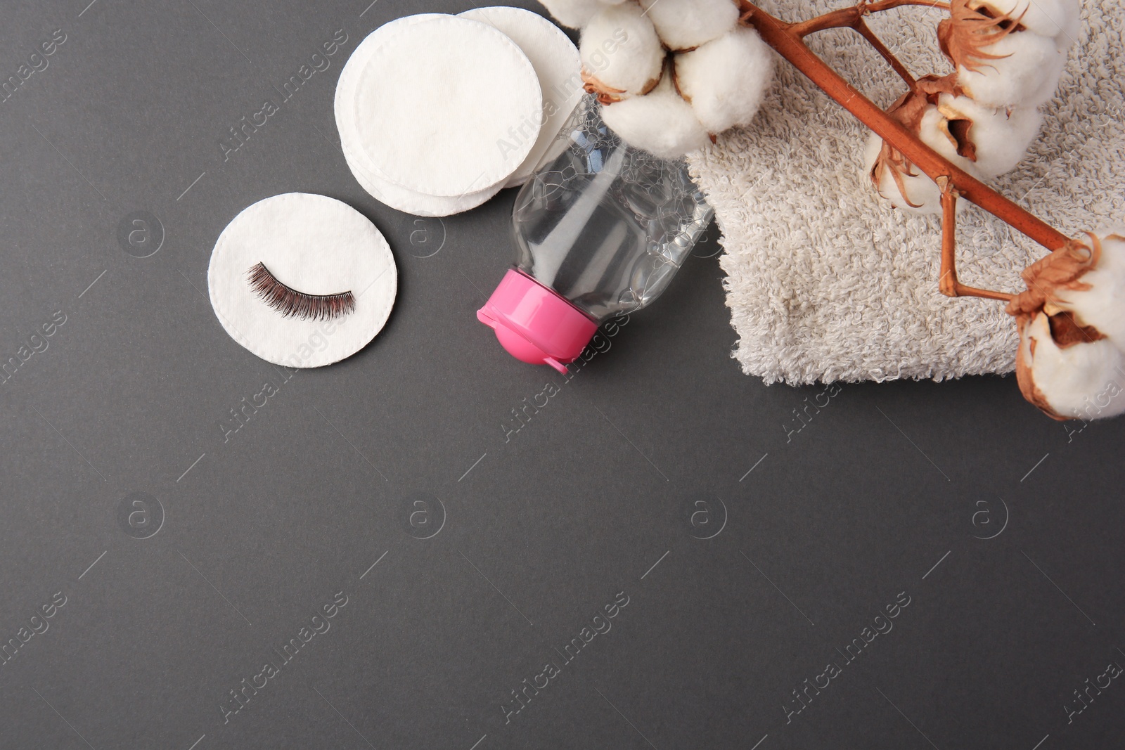 Photo of Bottle of makeup remover, cotton flowers, pads, towel and false eyelashes on grey background, flat lay. Space for text