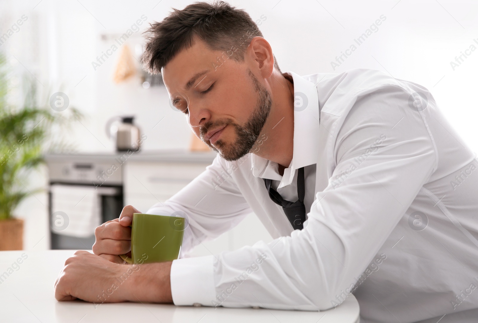 Photo of Sleepy man with cup of drink at home in morning