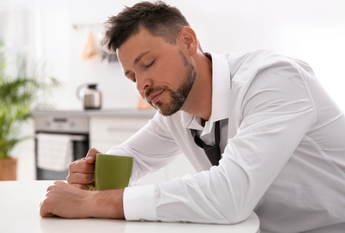 Sleepy man with cup of drink at home in morning