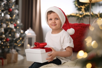 Photo of Cute little boy holding gift box on sofa in room decorated for Christmas