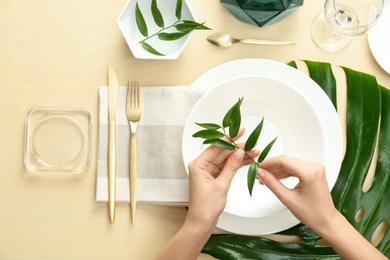 Woman setting table with green leaves for festive dinner, top view