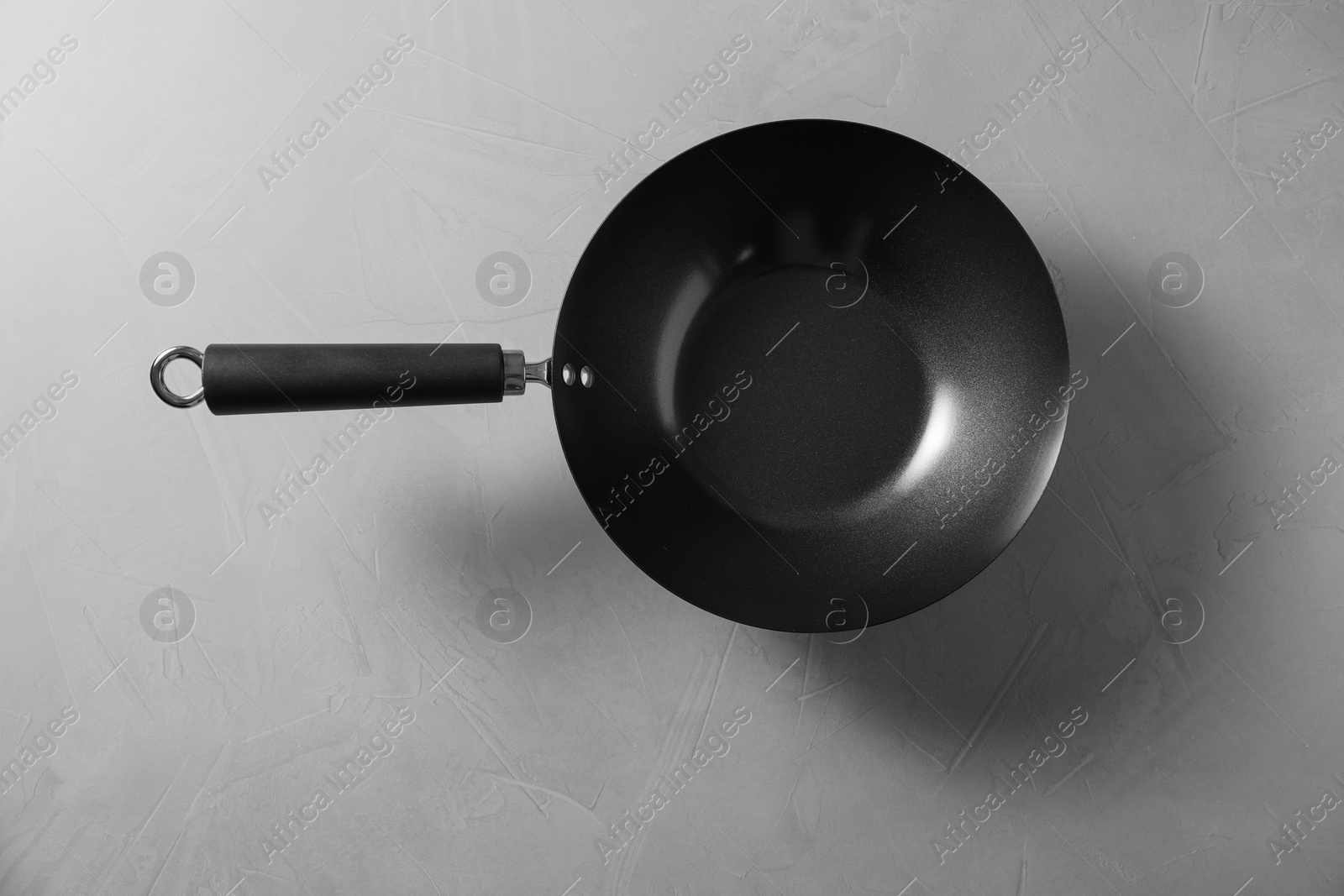 Photo of Empty iron wok on grey textured table, top view. Chinese cookware