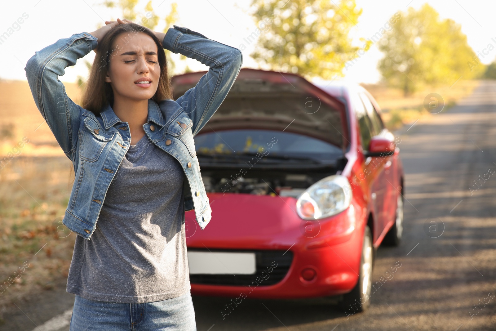 Photo of Stressed young woman near broken car outdoors