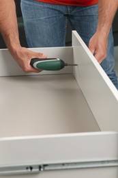 Photo of Man with electric screwdriver assembling drawer, closeup