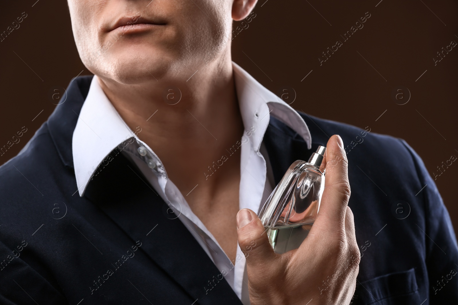 Photo of Handsome man in suit using perfume on dark background, closeup