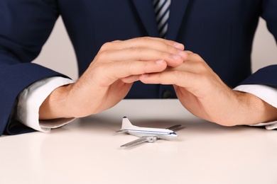 Photo of Insurance agent covering toy plane at table, closeup. Travel safety concept