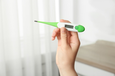 Photo of Woman with modern digital thermometer indoors, closeup