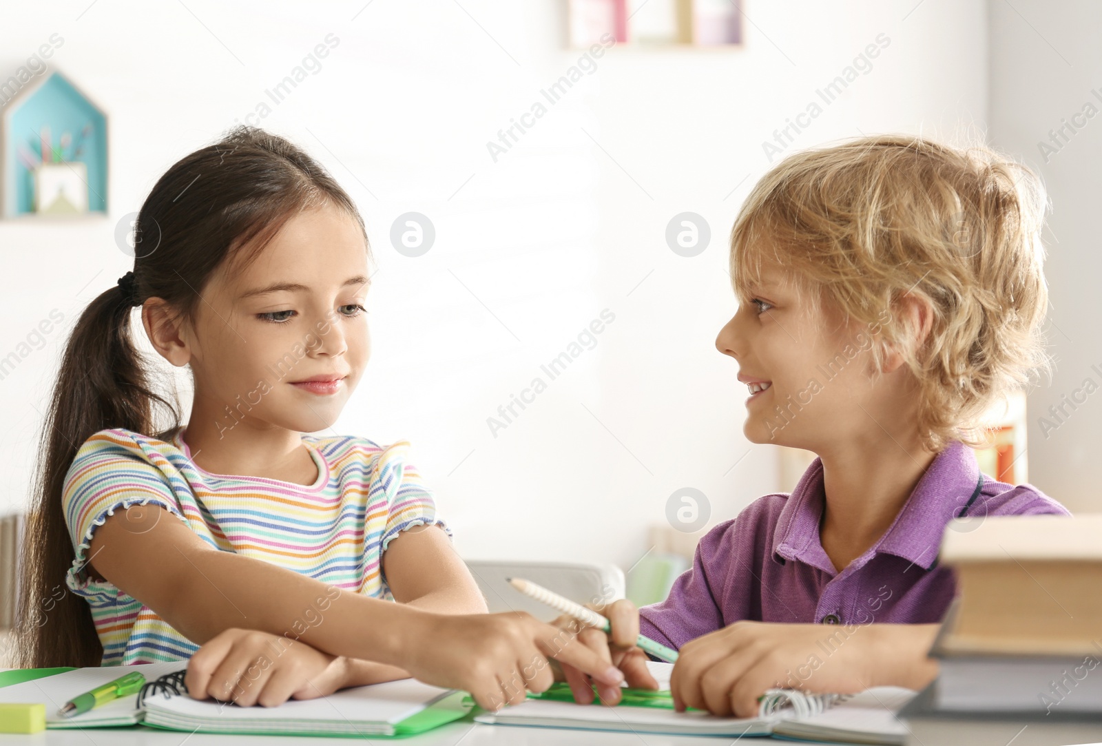Photo of Little boy and girl doing homework at table indoors