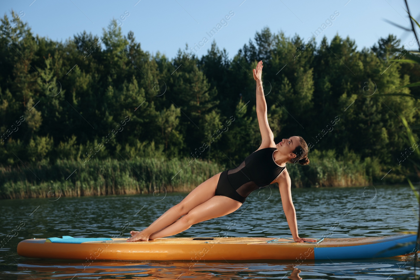 Photo of Young woman practicing yoga on color SUP board on river