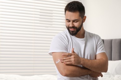 Photo of Man with dry skin applying cream onto his arm indoors, space for text