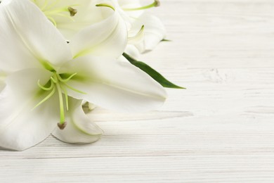 Beautiful lily flowers on white wooden table, closeup. Space for text