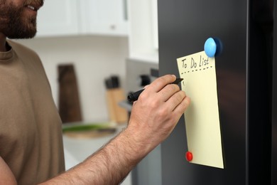 Man writing to do list on refrigerator door in kitchen, closeup