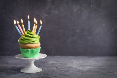 Photo of Stand with delicious birthday cupcake with burning candles on table