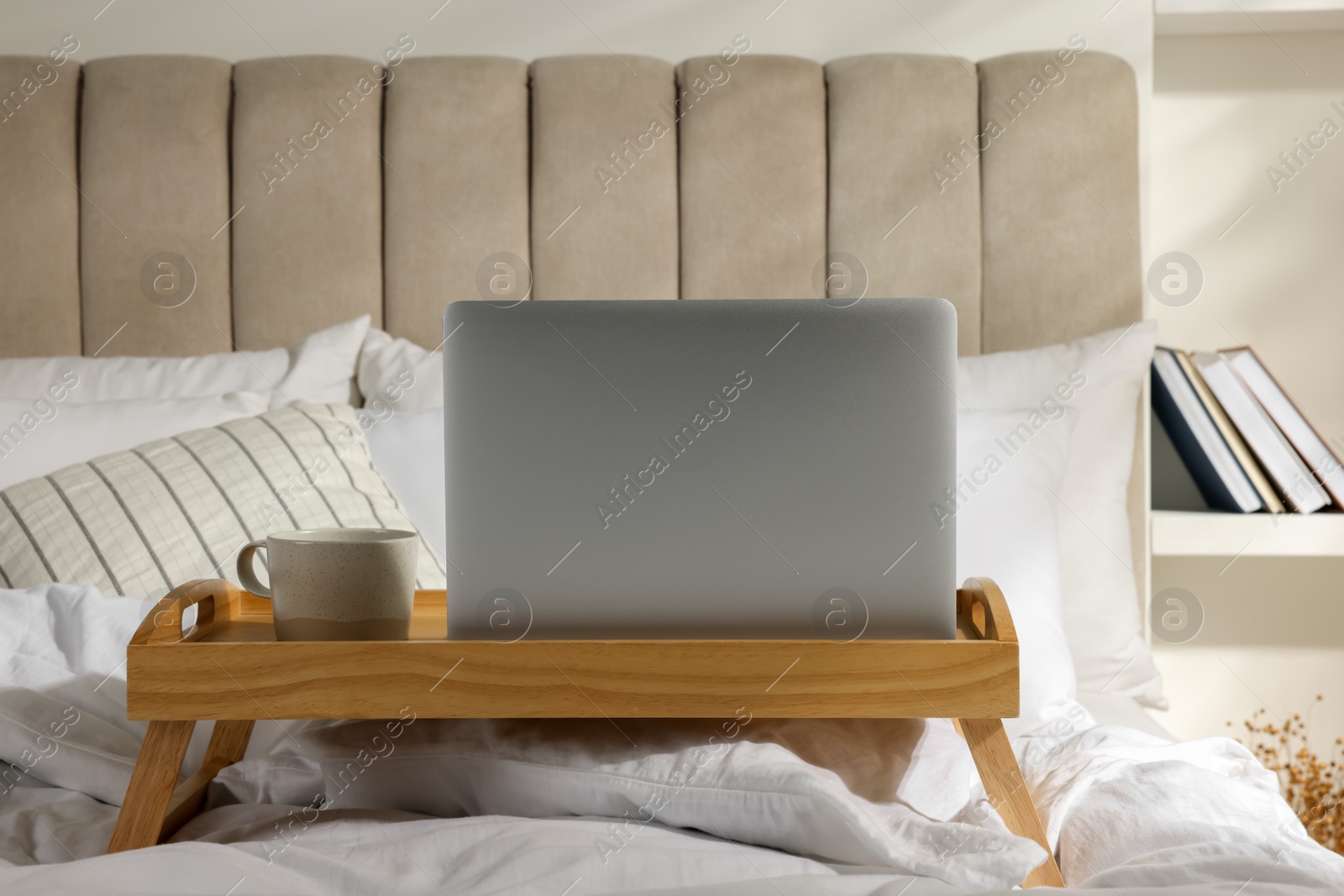 Photo of Wooden tray with modern laptop and cup of aromatic drink on bed indoors