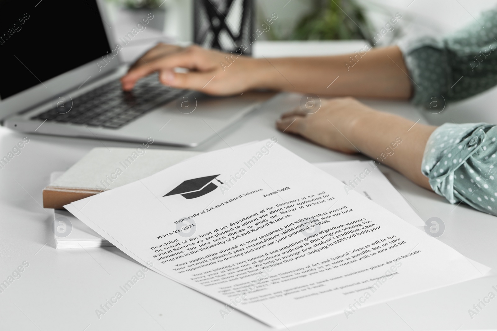 Photo of Student working with laptop at white table indoors, focus on acceptance letters from universities