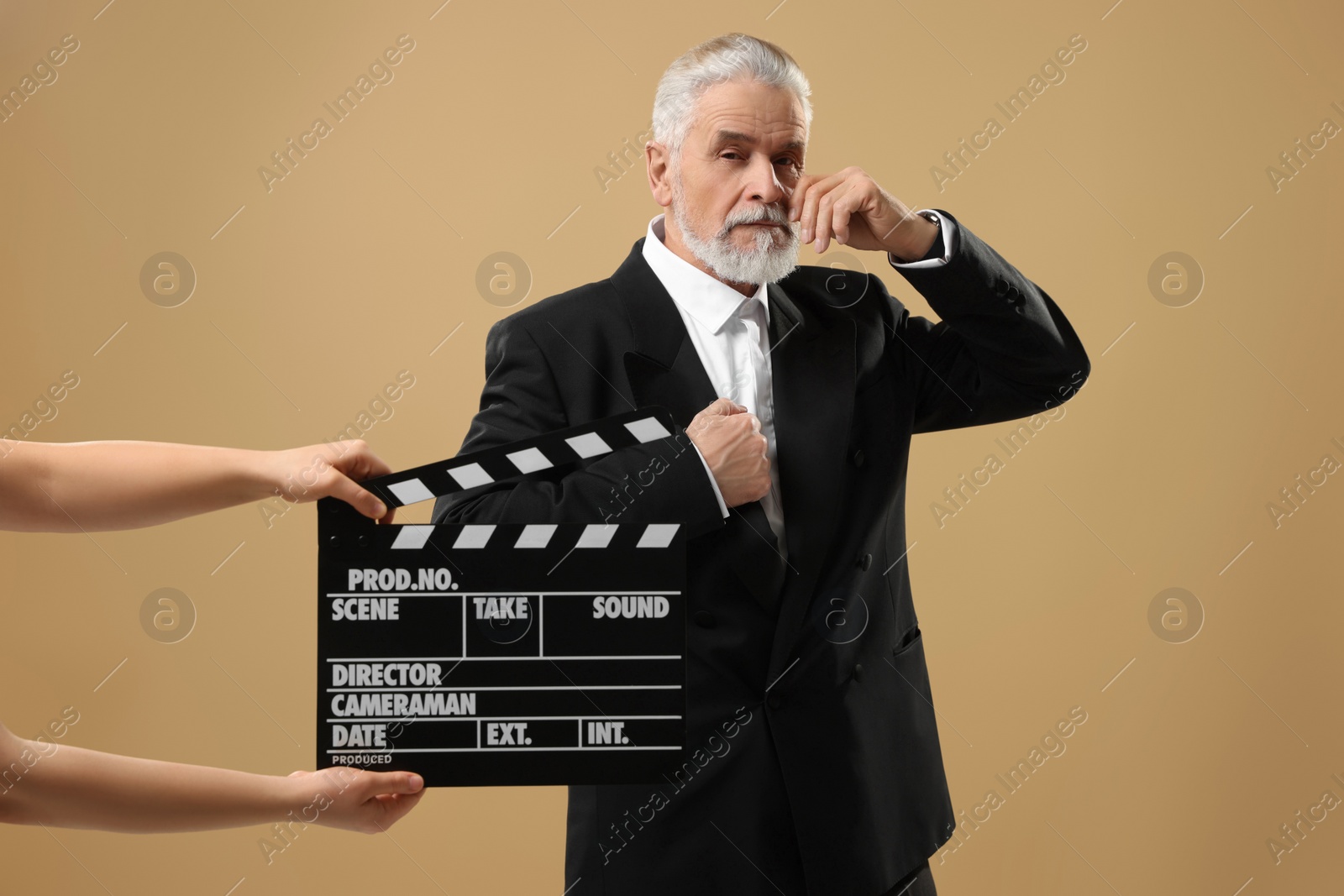 Photo of Senior actor performing role while second assistant camera holding clapperboard on beige background. Film industry