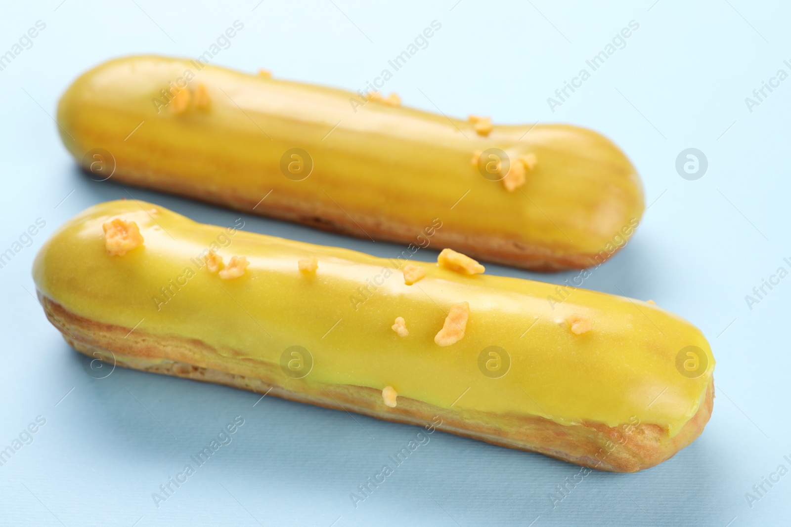 Photo of Delicious eclairs covered with glaze on light blue background